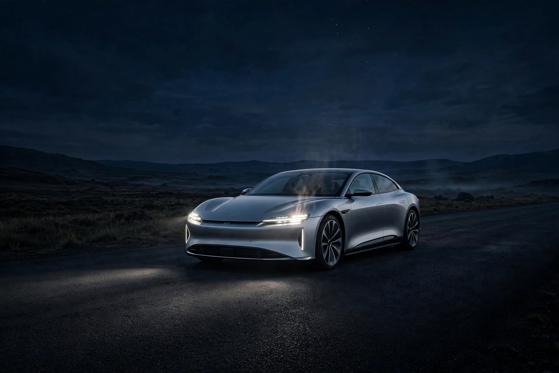 Silver Lucid Air electric sedan on a dark desert road at night, headlights glowing