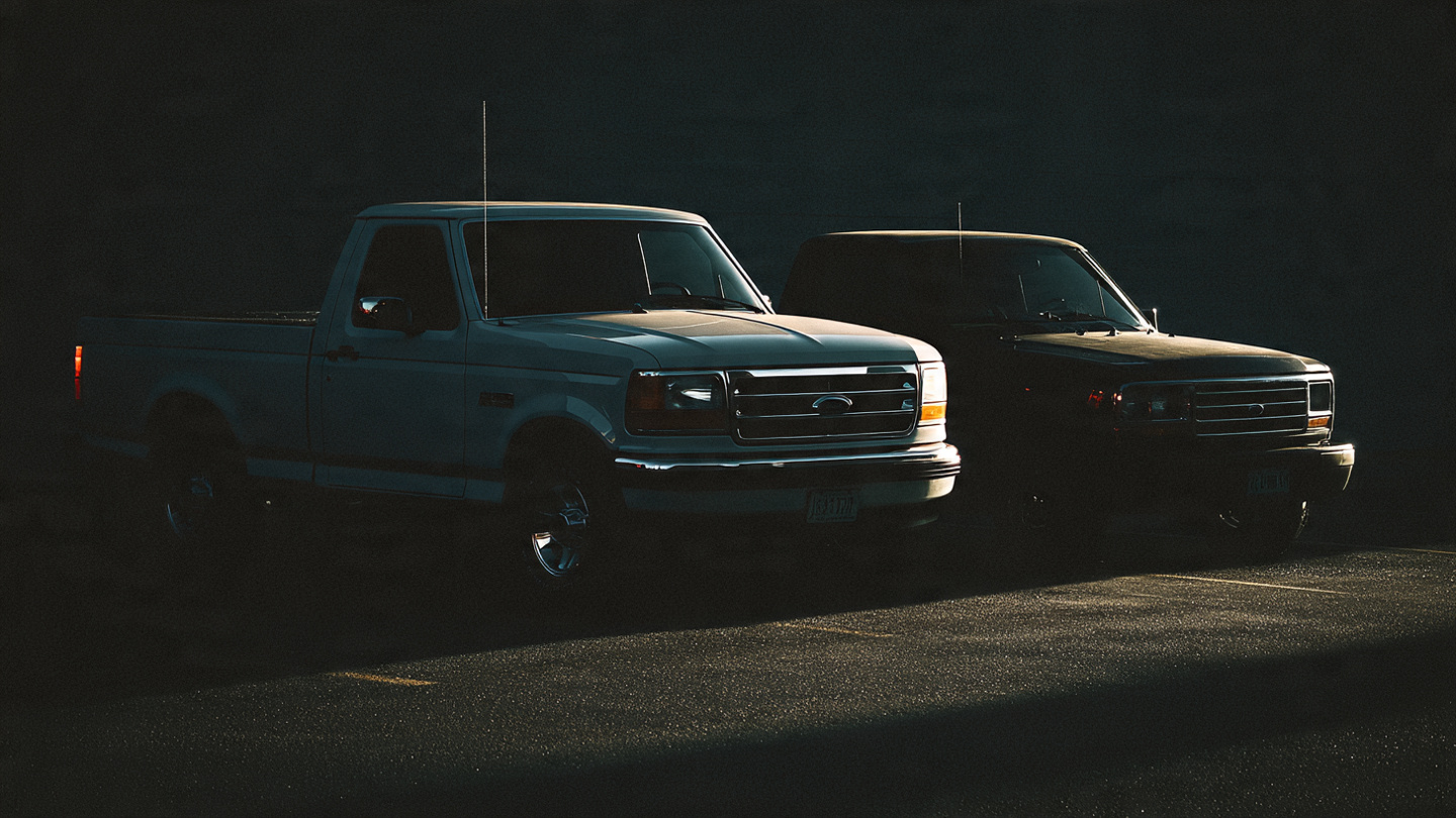 Two pickup trucks in shadowy parking lot showing the vehicle safety gap in truck deaths from FARS data