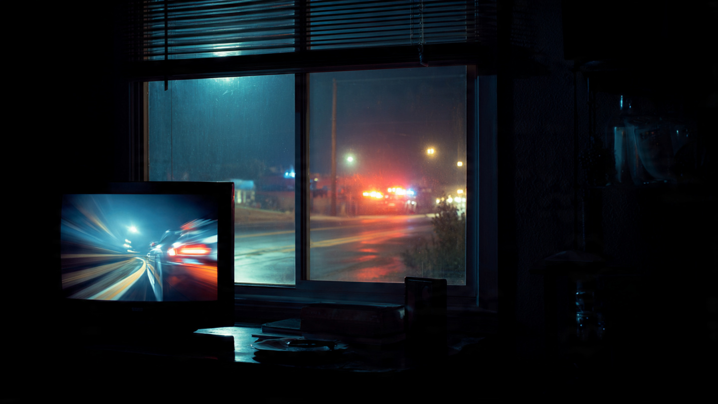 A dark living room with a TV showing a sports car commercial while emergency lights flash through the window