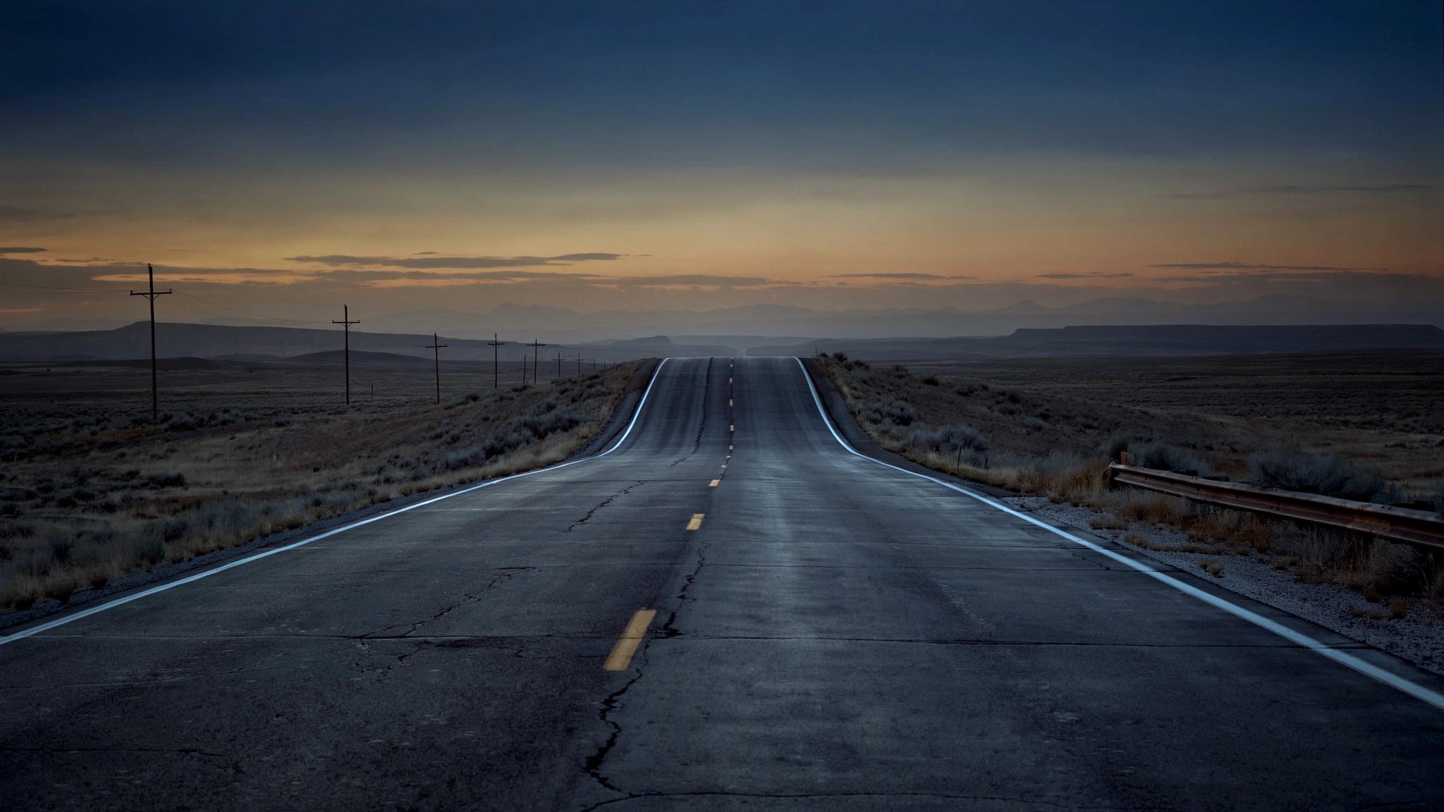 Empty American highway stretching to vanishing point at dusk, centerline stripe fading into amber horizon