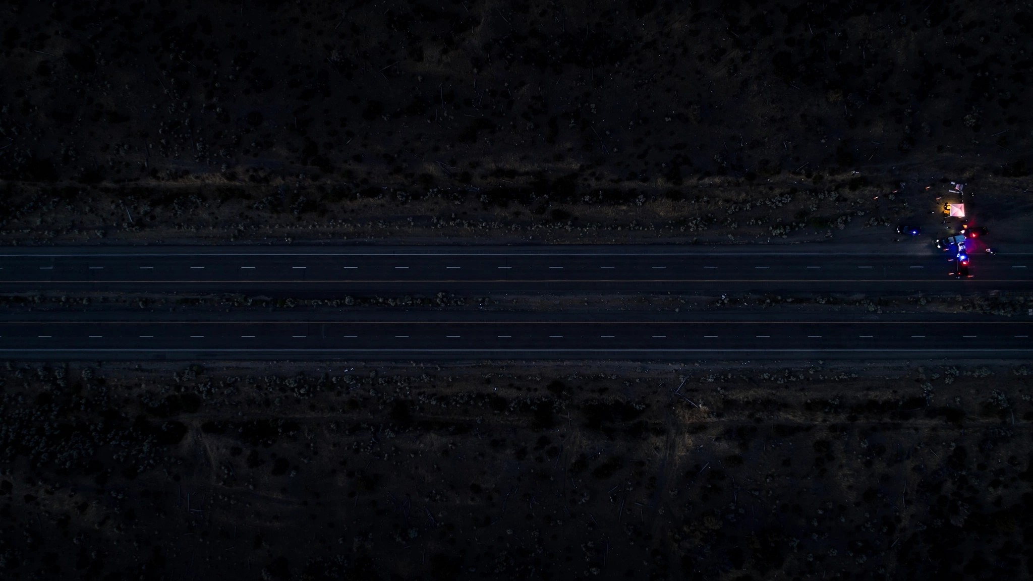 An empty highway stretching into the distance at night with distant police checkpoint lights barely visible